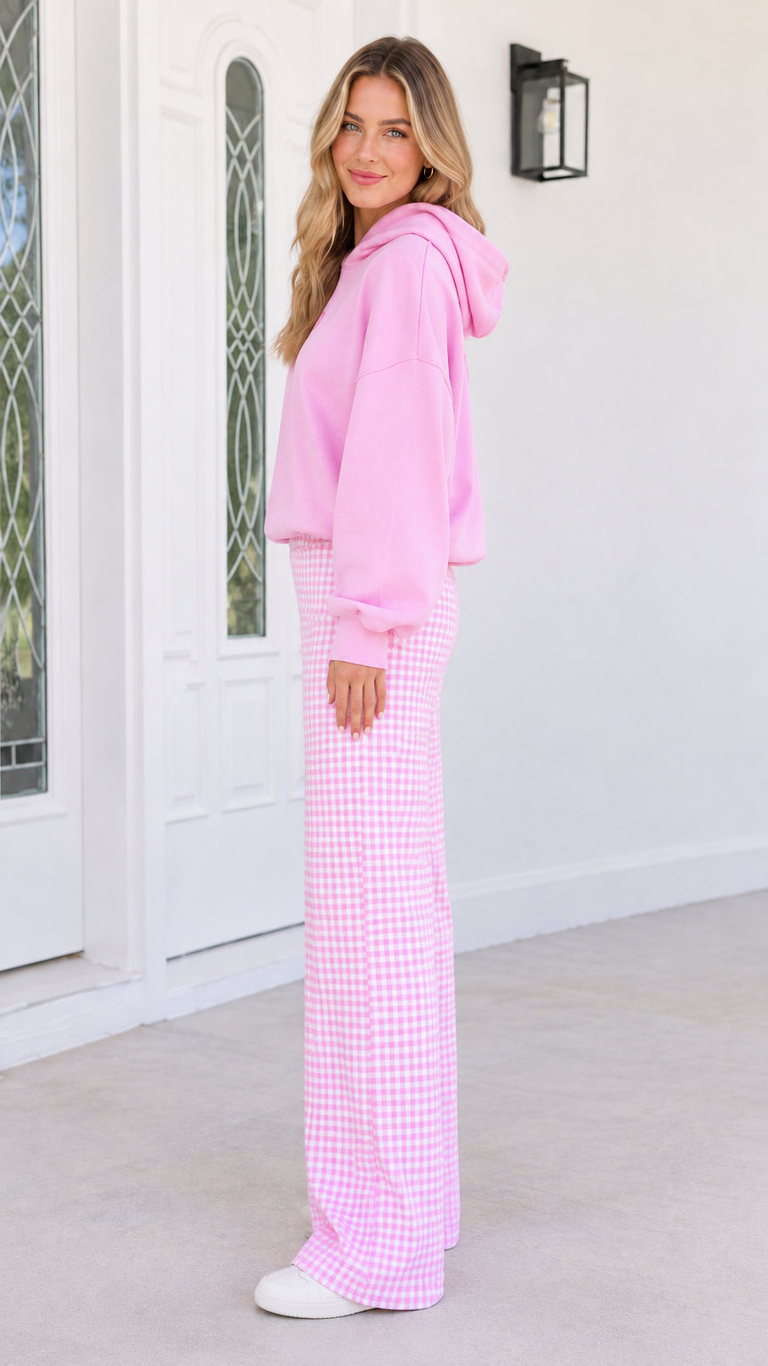 Side profile view of woman wearing pink hoodie and high-waist gingham trousers