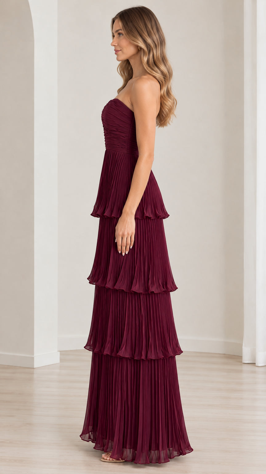 Side profile view of strapless burgundy tiered pleated gown