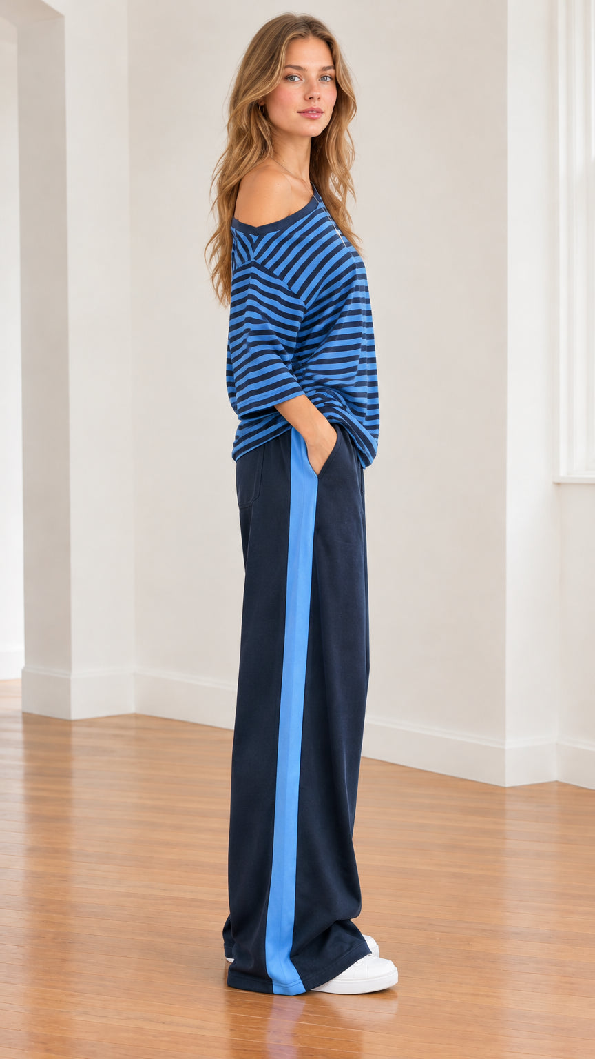 Side profile of model showing relaxed fit and vertical light blue side stripe on navy trousers