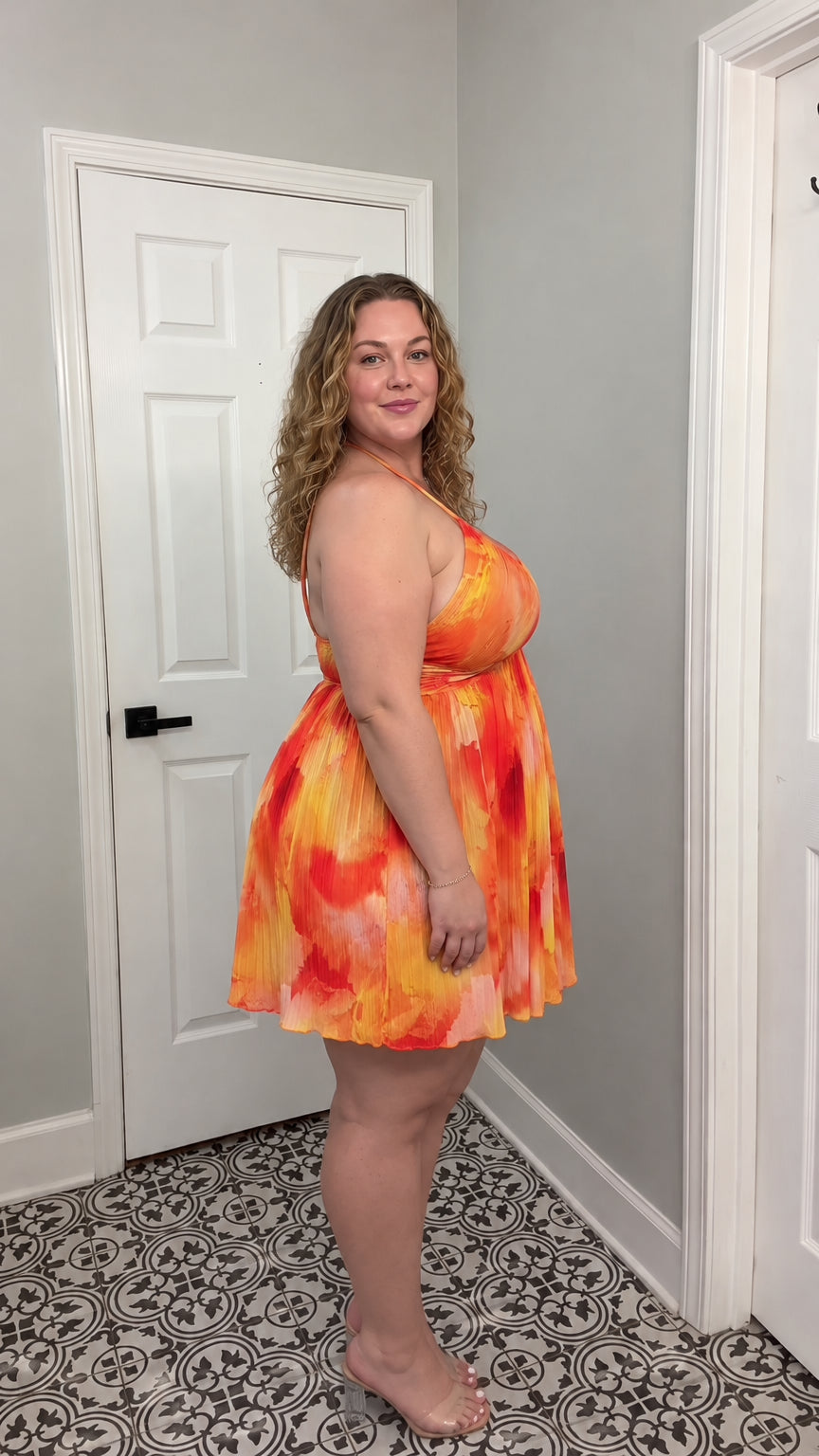 Side profile of model wearing orange abstract printed pleated halter mini dress