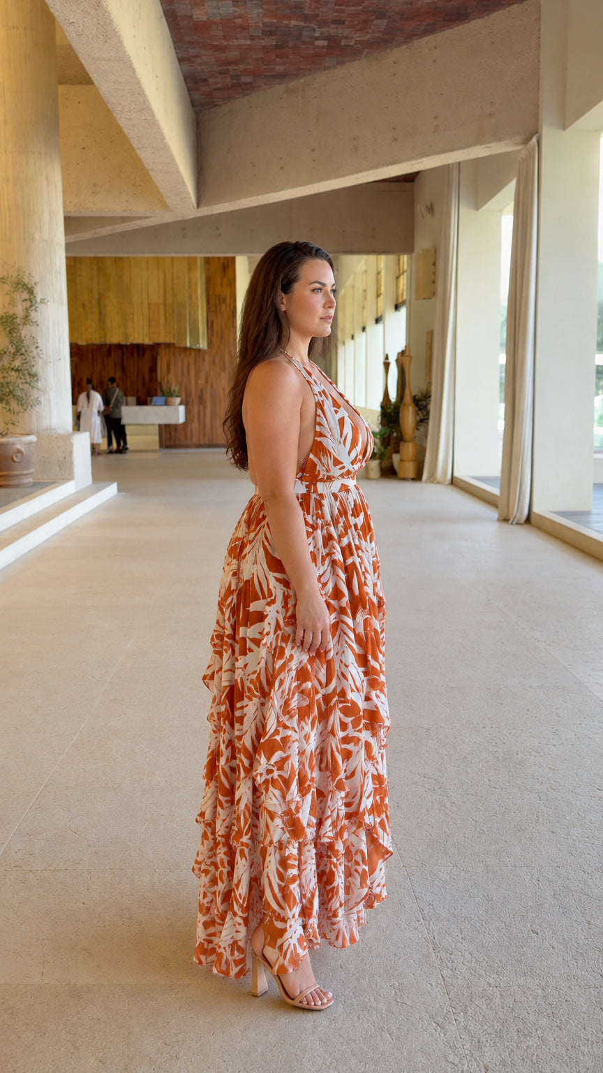 Side angle view of woman wearing rust orange tropical halter tiered ruffle maxi dress