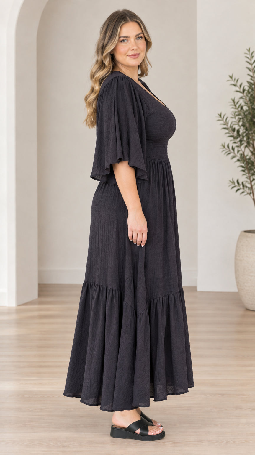 Side profile view of model wearing black flutter sleeve tiered maxi dress