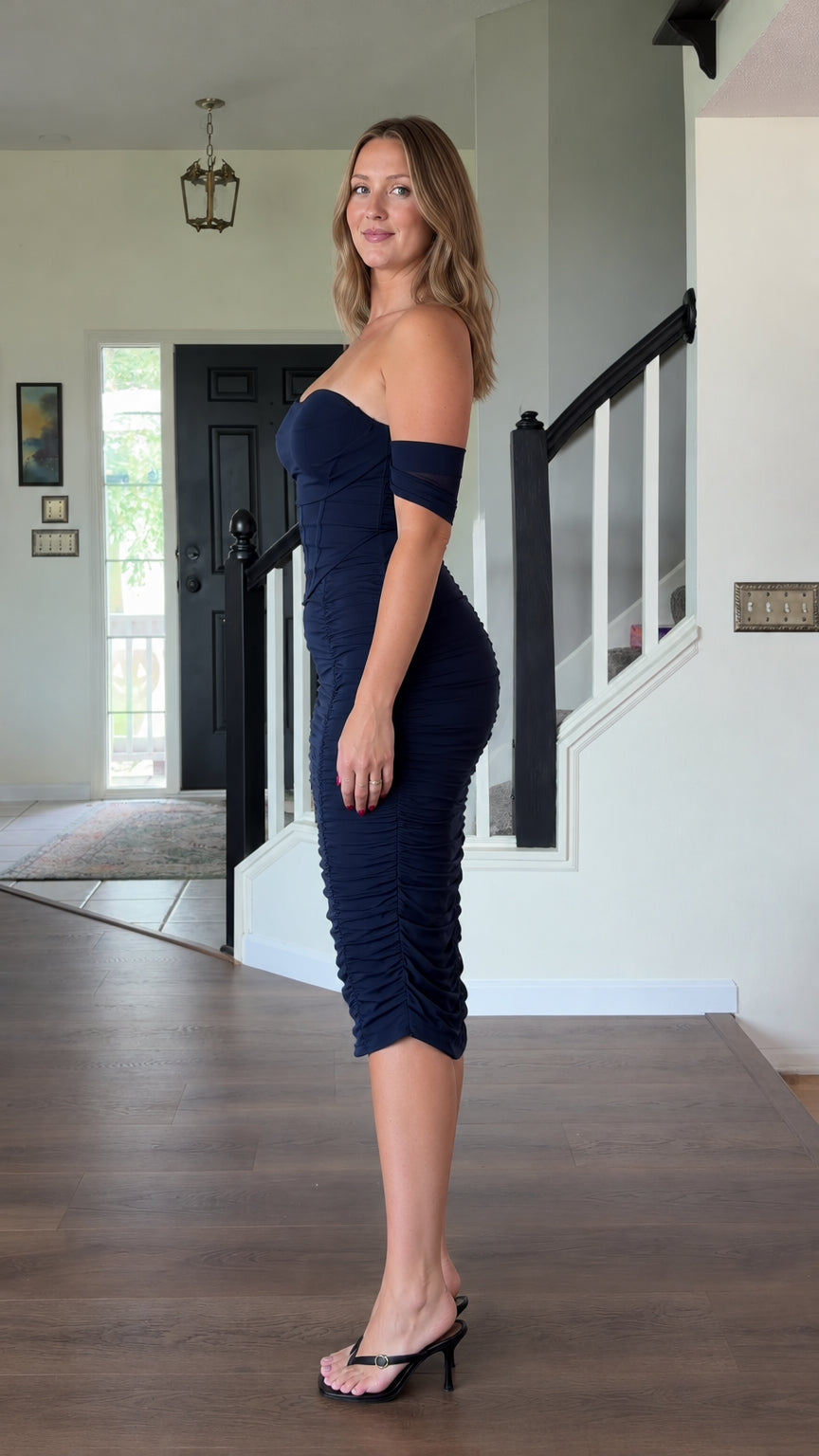 Side profile view of woman wearing navy blue off-the-shoulder corset ruched midi dress