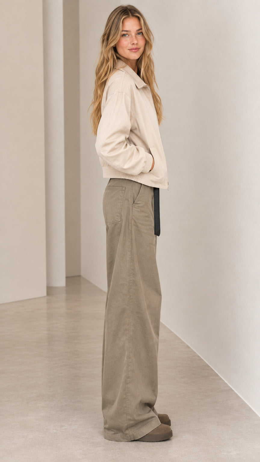 Side profile view of woman wearing beige cropped zip jacket and relaxed wide-leg trousers