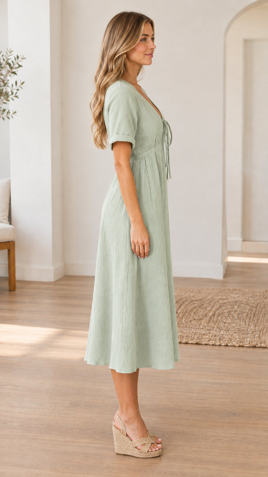 Side profile view of woman wearing sage green short sleeve front-tie midi dress with wedge heels