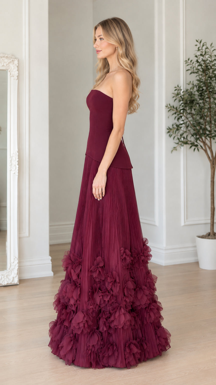 Side profile view of strapless burgundy pleated formal dress with textured petal skirt