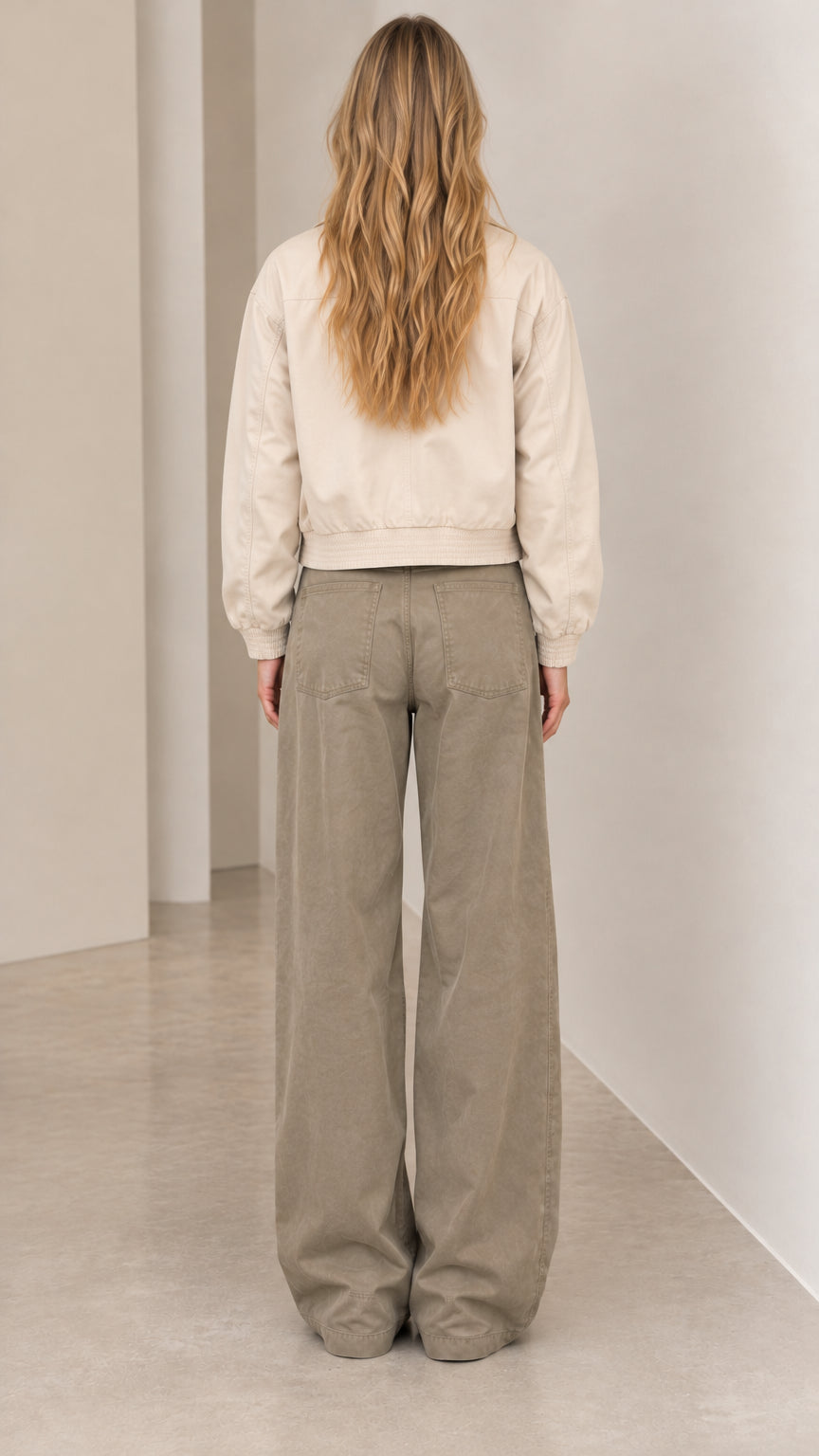 Back view of woman wearing beige collared jacket with elastic hem and wide-leg trousers