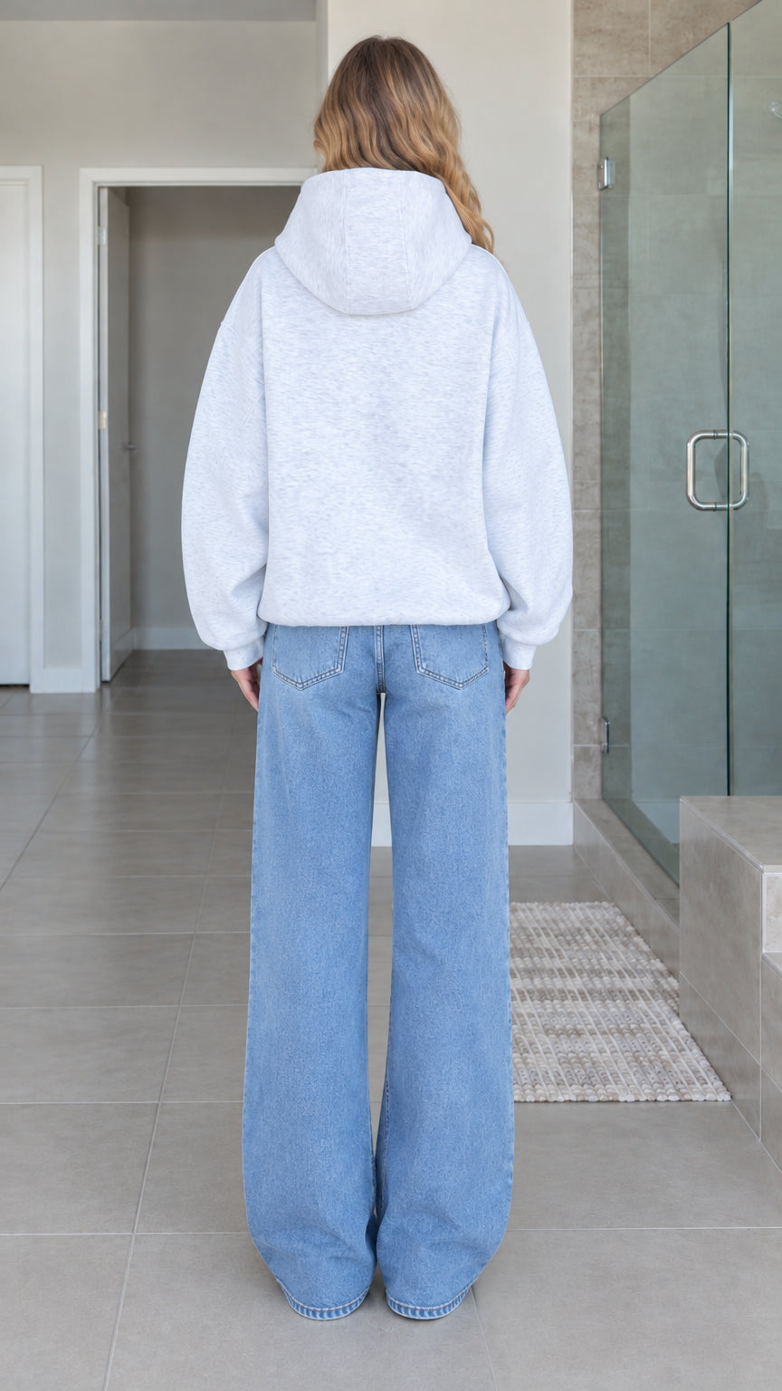 Back view of model wearing heather grey oversized zip-up fleece hoodie with drop shoulders and hood