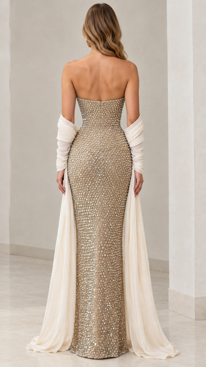 Rear back view of model wearing strapless rhinestone evening gown with flowing back drapes