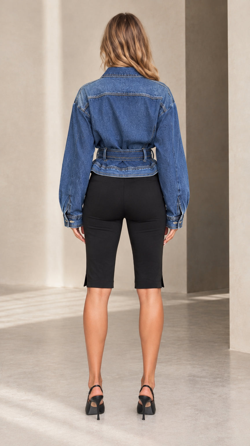 Back view of model showing the cinched back and yoke of the blue belted denim jacket