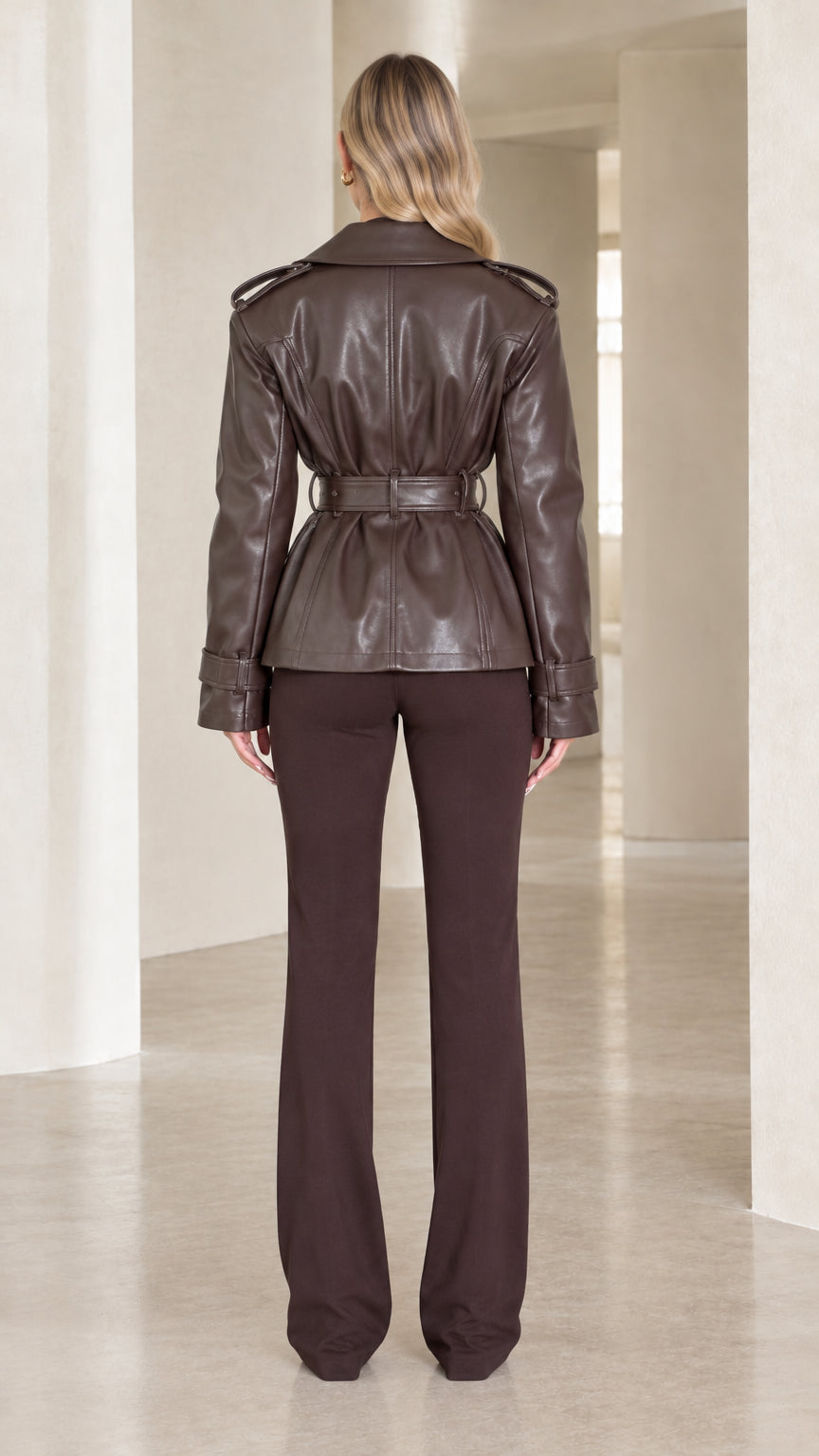 Back view of model wearing dark brown belted faux leather jacket highlighting clean tailored lines