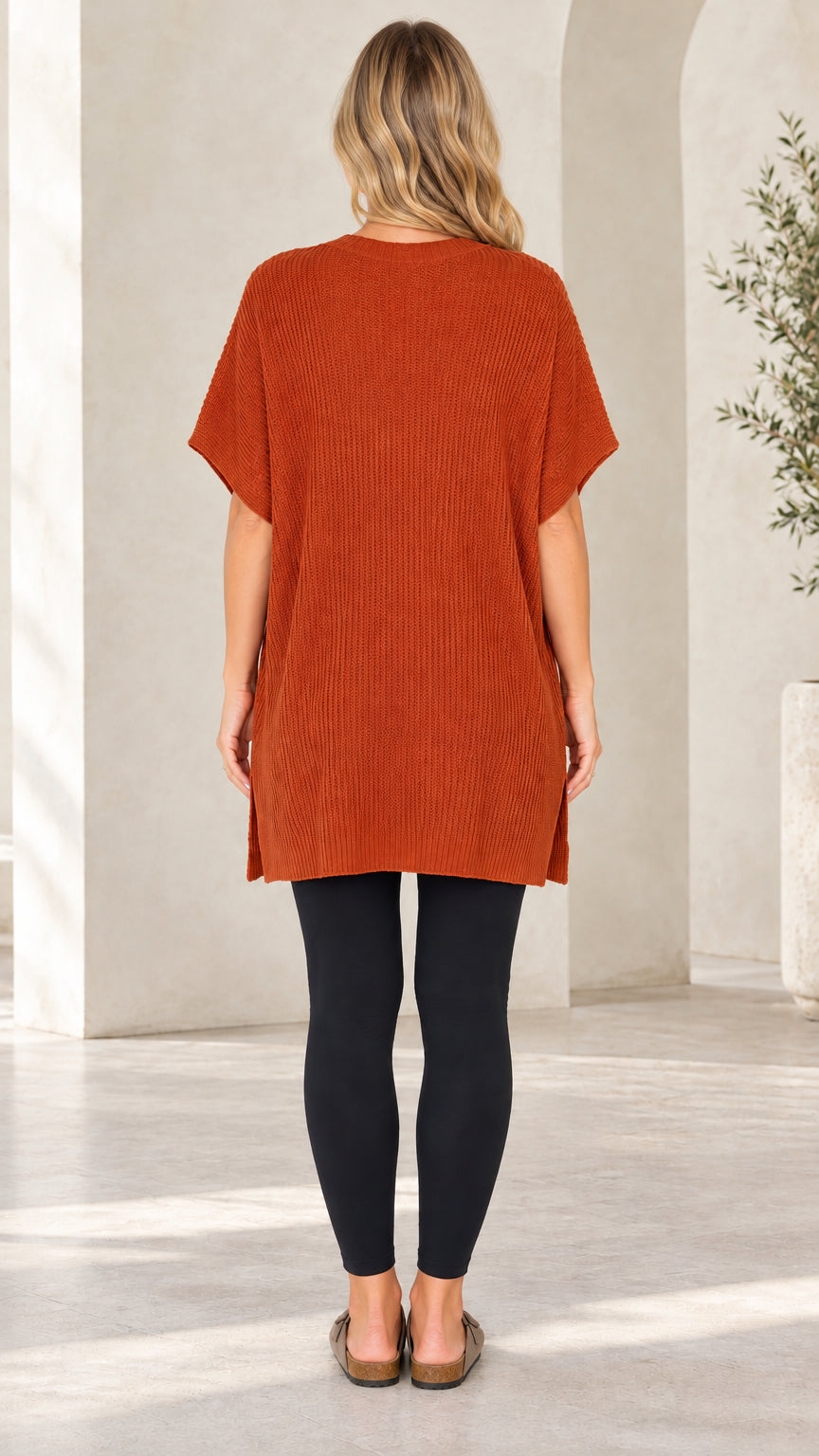 Back view of rust short sleeve ribbed knit tunic sweater over black leggings