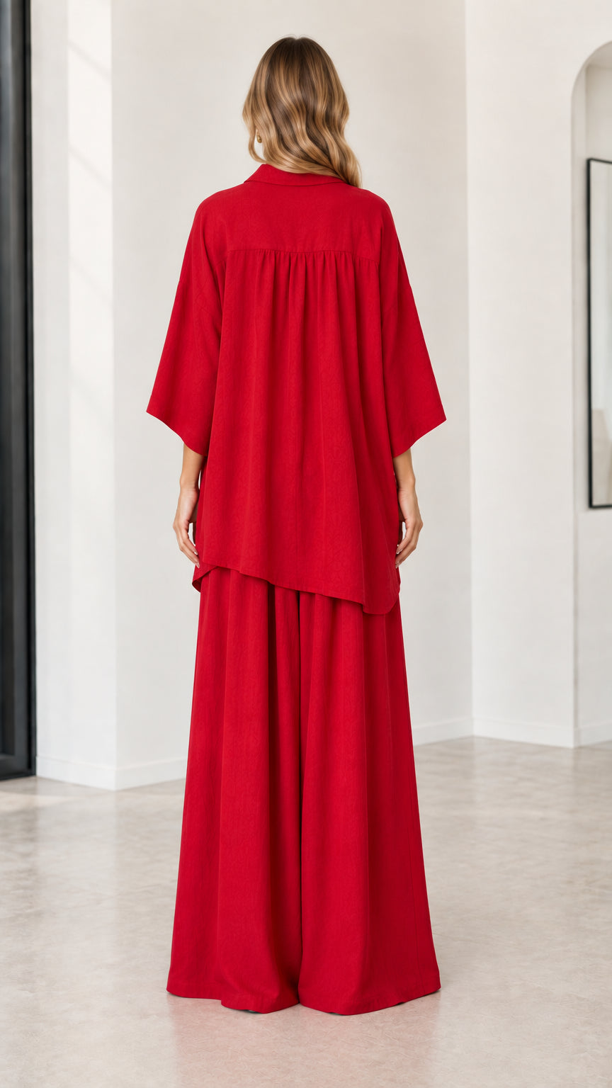 Back full-length view of woman wearing red oversized shirt and pleated wide-leg pants