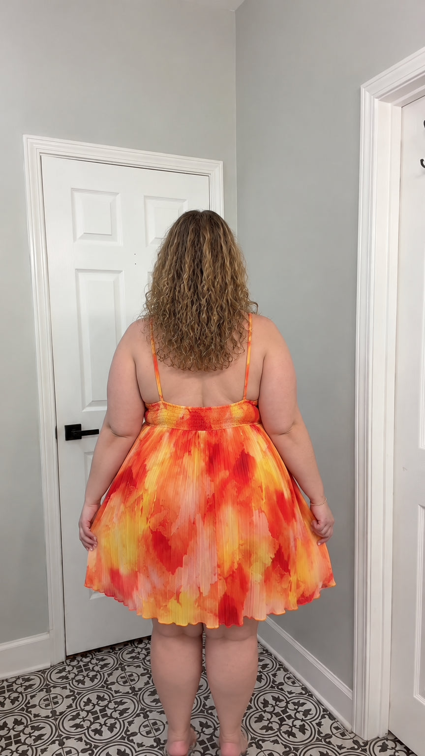 Back view of model showing open back and smocked bodice on orange pleated halter dress