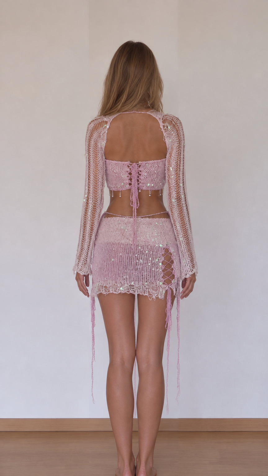 Back view of model showcasing open-back knit shrug and pink lace-up micro mini skirt