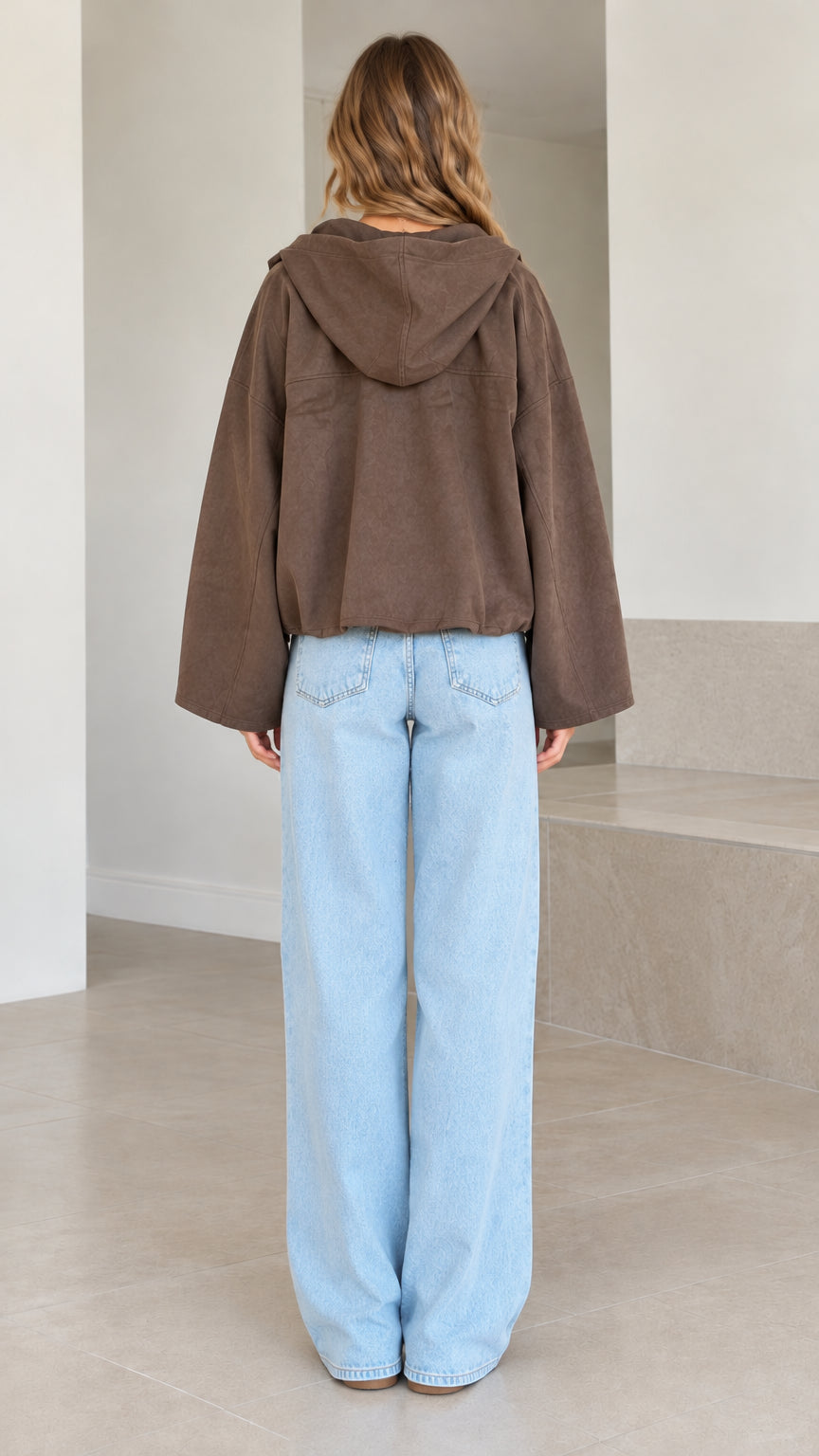 Back view of model in brown cropped jacket highlighting the attached hood and boxy drape