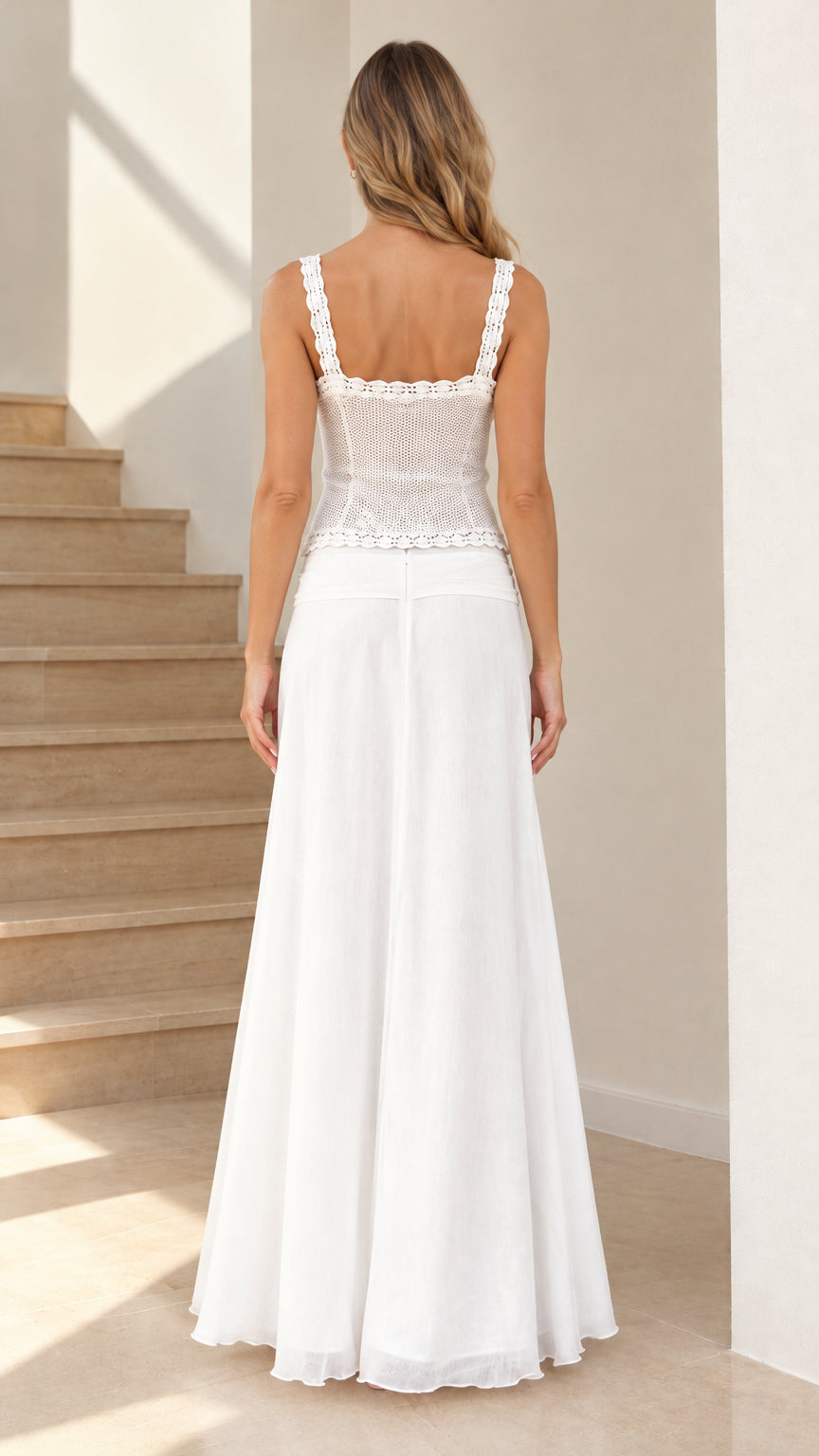Back view of model in white lace camisole top with wide straps and long white flowing skirt