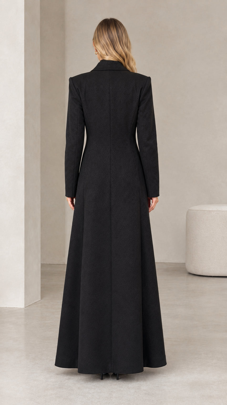 Back view of woman wearing black floor-length tailored maxi coat with flared hem