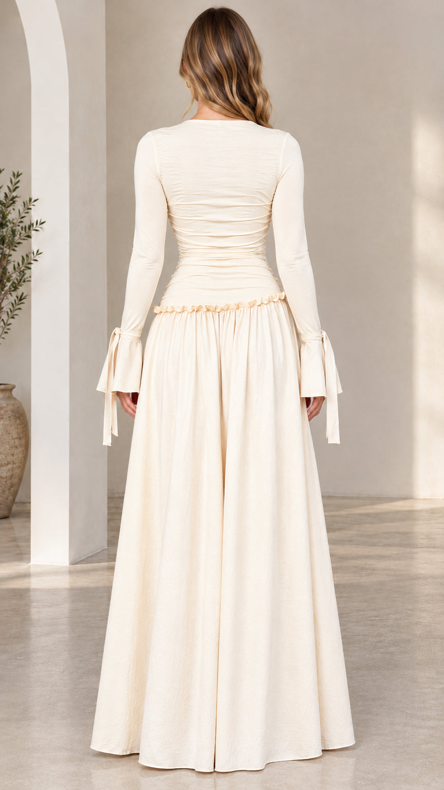 Back full-length view of woman wearing cream ruched maxi dress with flared cuffs