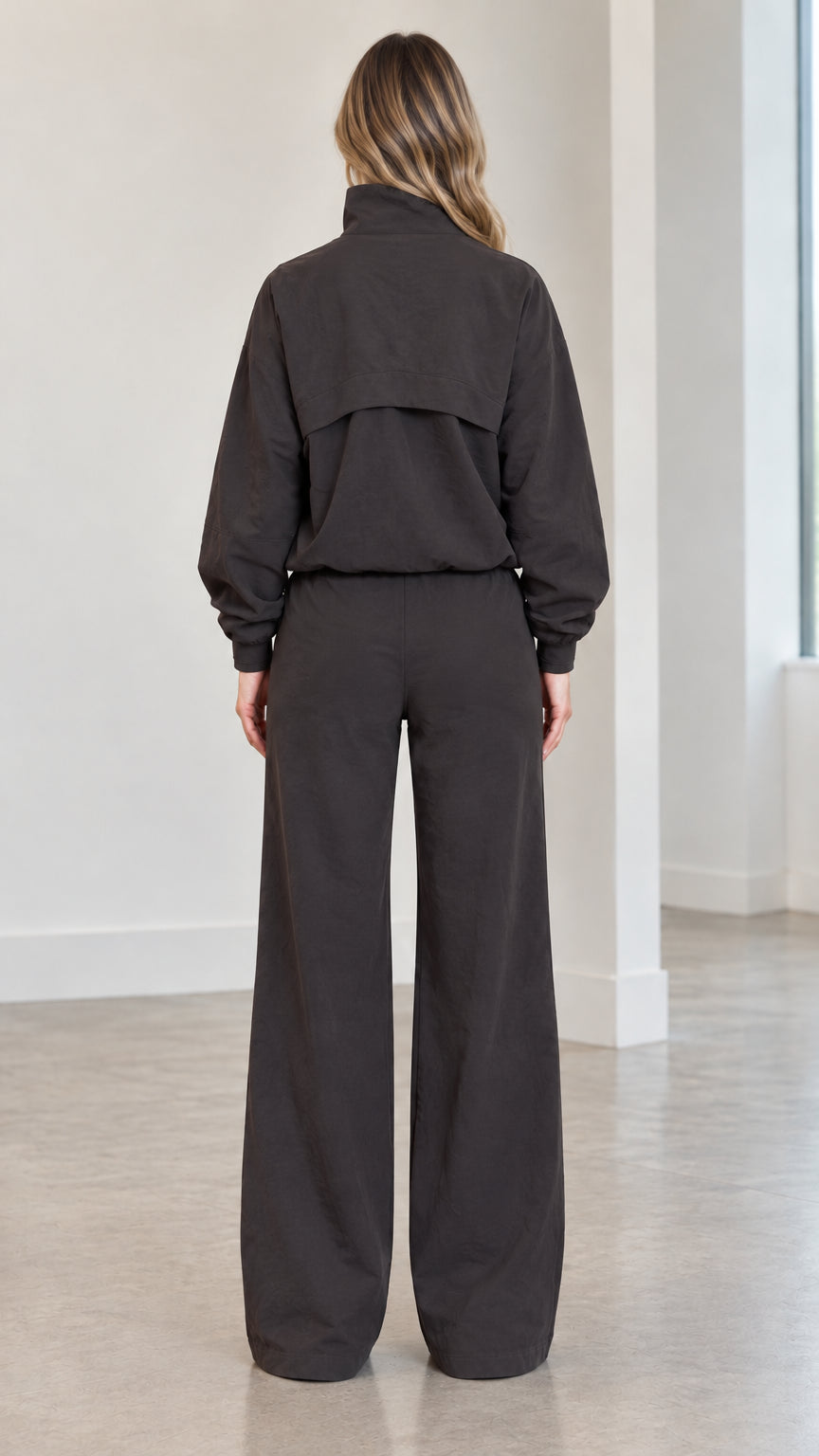 Back view of woman wearing charcoal track jacket with back storm-flap detailing and matching wide-leg pants