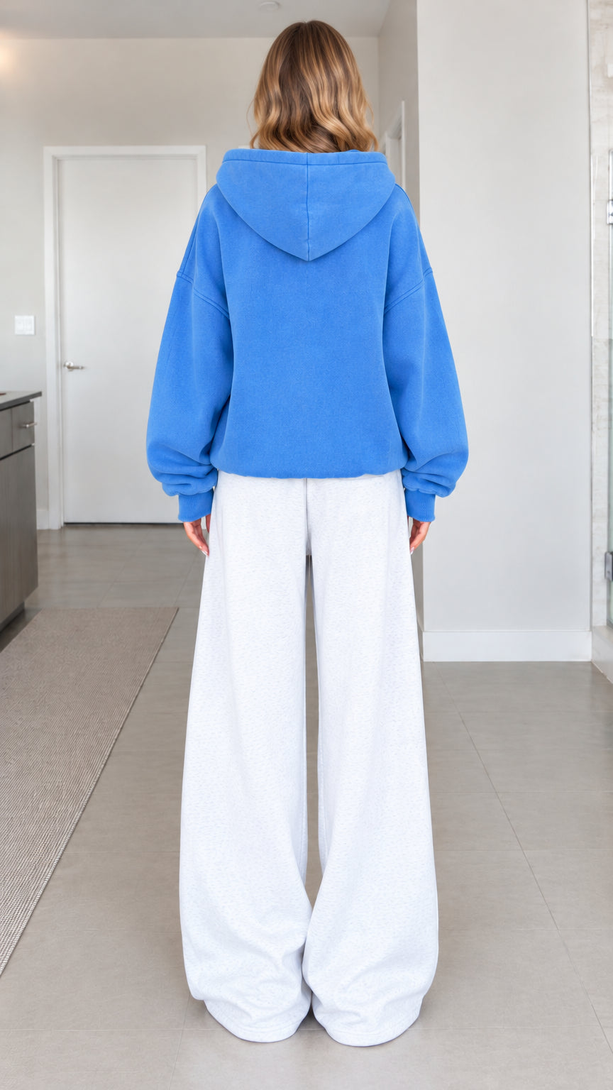 Back full-length view of a woman in an oversized blue zip-up hoodie featuring a spacious hood