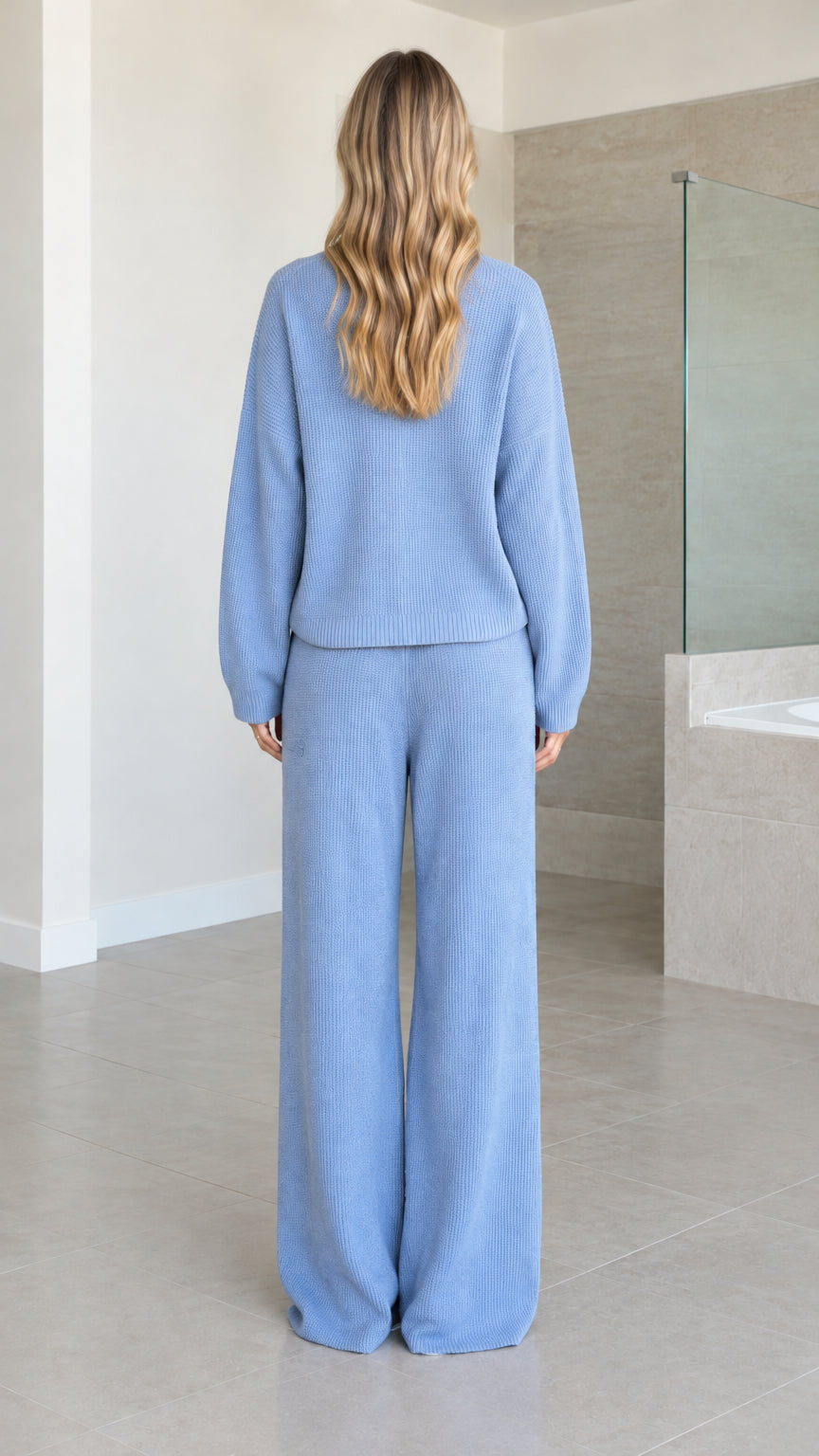 Back view of woman wearing Light Blue ribbed knit zip jacket and wide-leg trousers