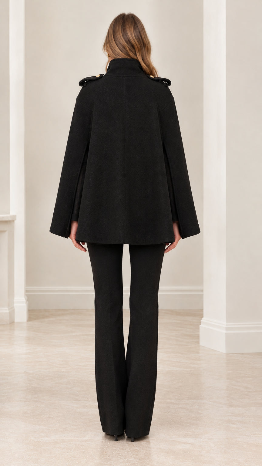 Back view of model wearing black structured cape coat with high collar