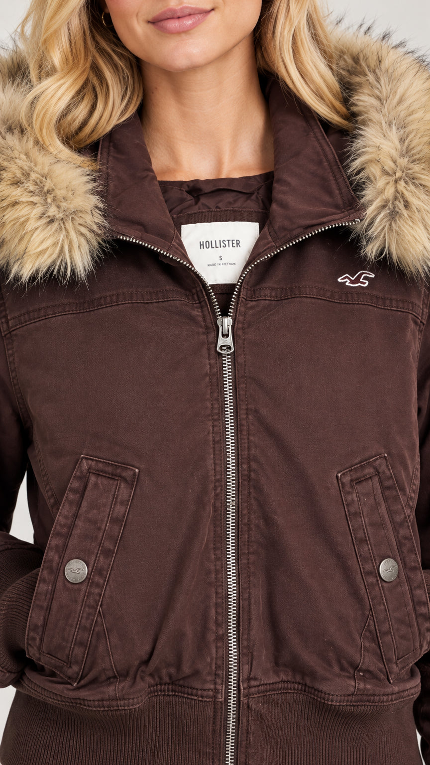 Close-up detail of brown jacket zipper, snap pocket, and faux fur hood trim