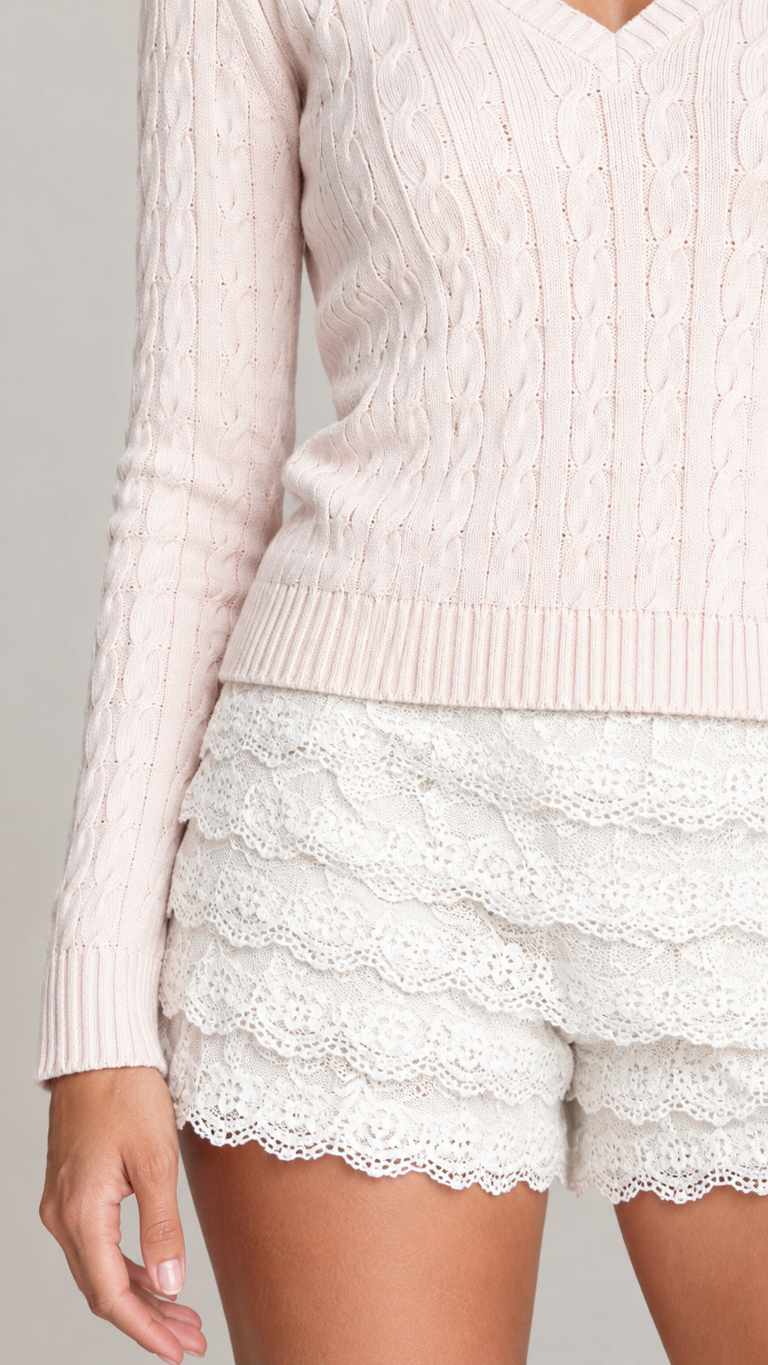 Close-up detail of cable knit sweater sleeve and tiered floral lace shorts with scalloped edging