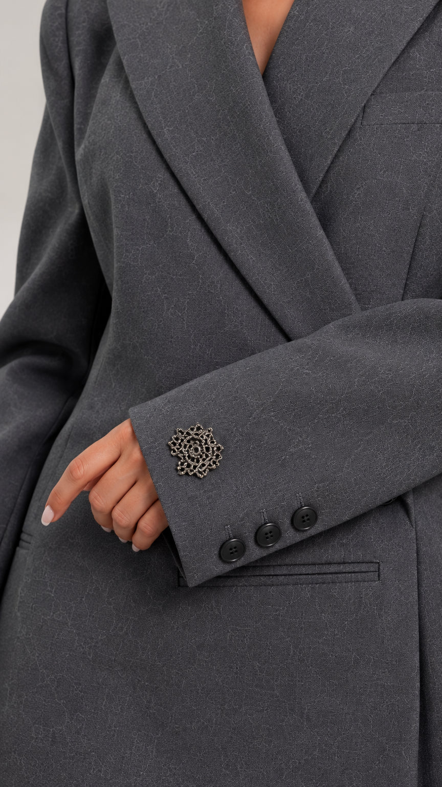 Close-up detail of blazer sleeve cuff with decorative brooch and buttons