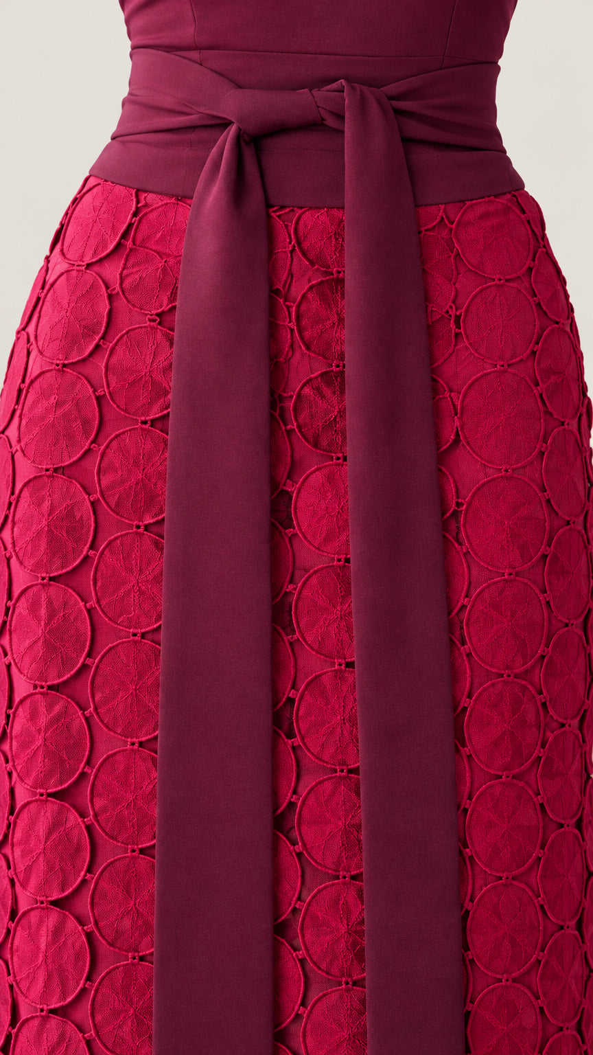 Close-up detail of berry red tie belt and intricate circular textured petal applique skirt