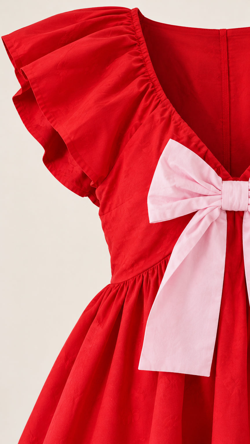 Close-up detail of red fabric, flutter shoulder ruffle, and pink front bow