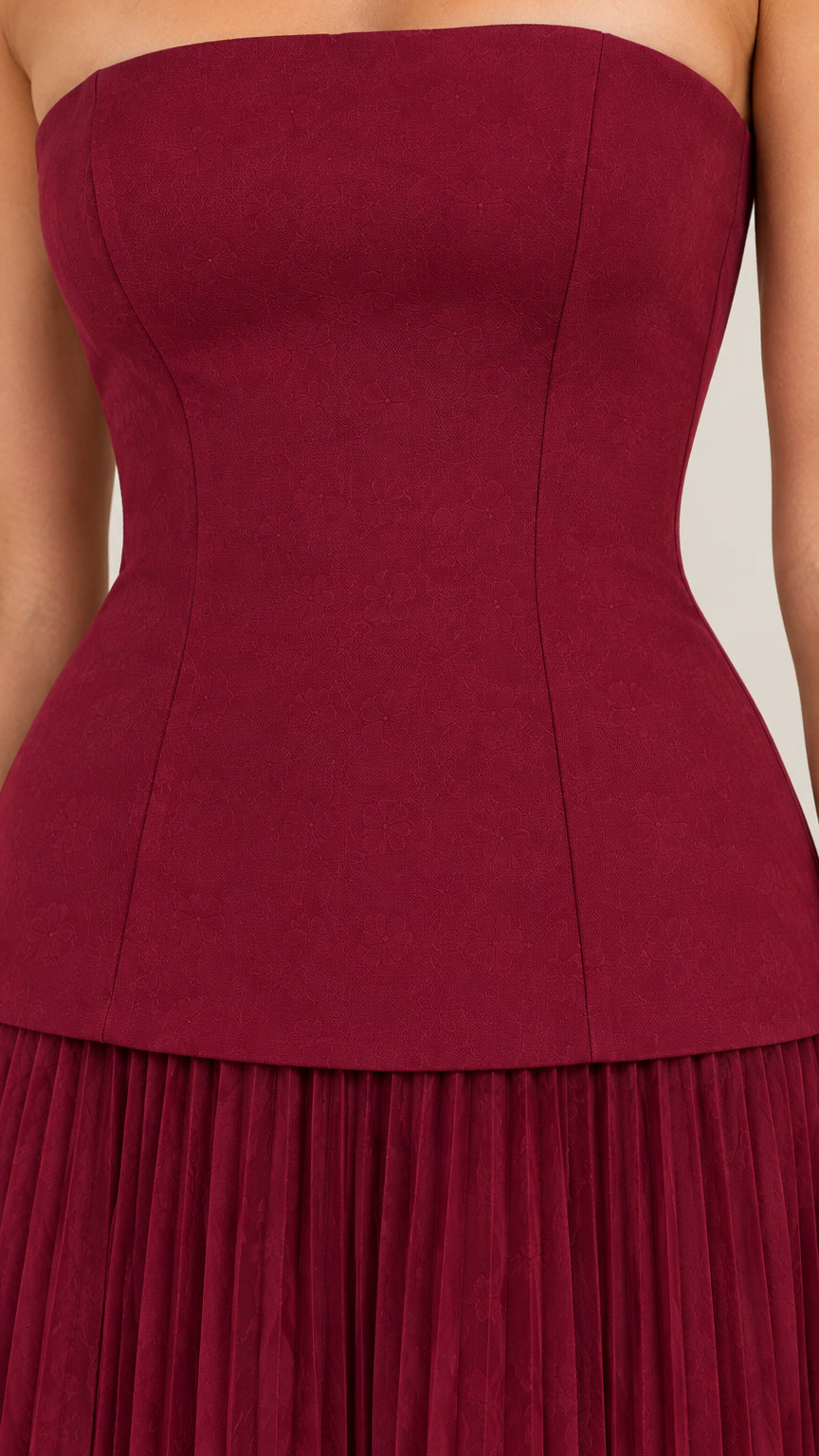 Close-up detail of structured burgundy corset bodice and drop waist pleated skirt seam