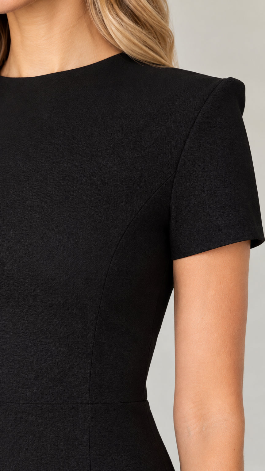 Close-up detail of Black mini dress showing high crew neckline, structured shoulder, and vertical bodice seam