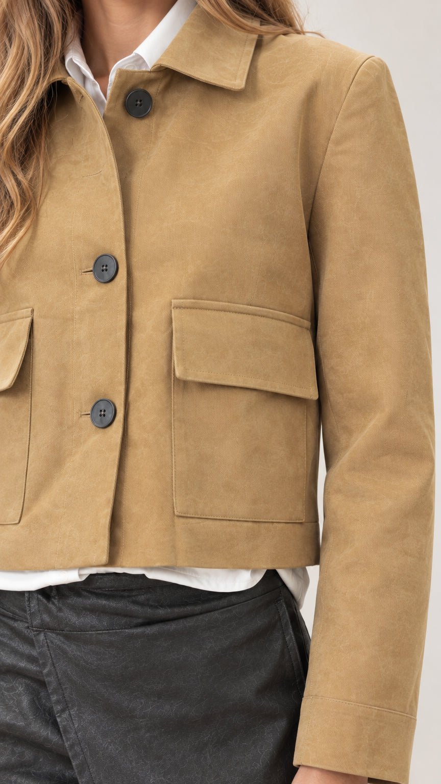 Close-up detail of tan cropped jacket showing button front closure, collar, and chest flap pocket