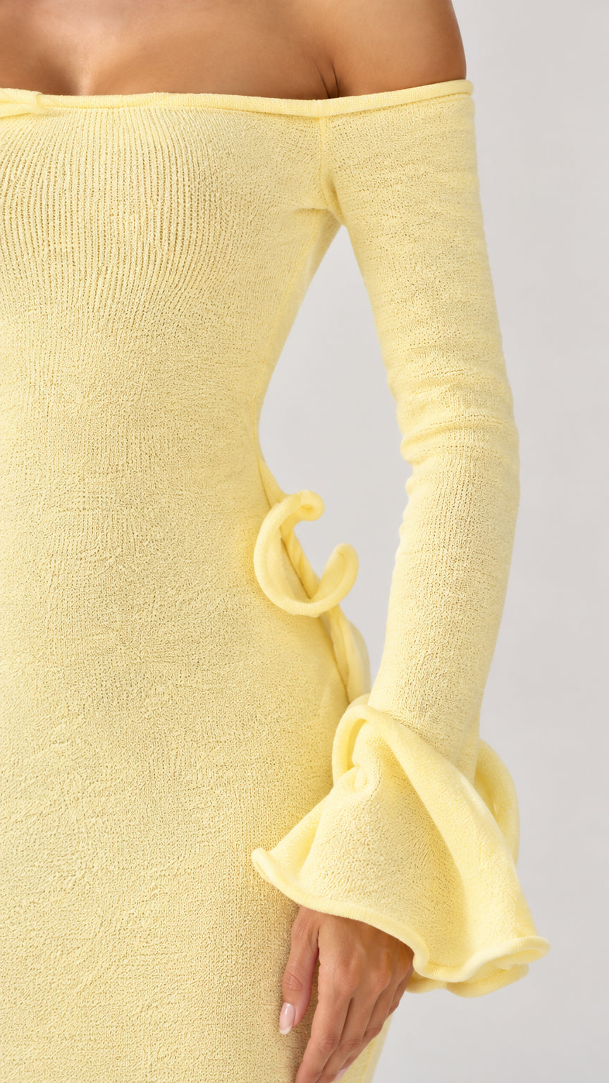 Close-up detail of ribbed knit fabric, side ruffle, and bell cuffs on pastel yellow gown
