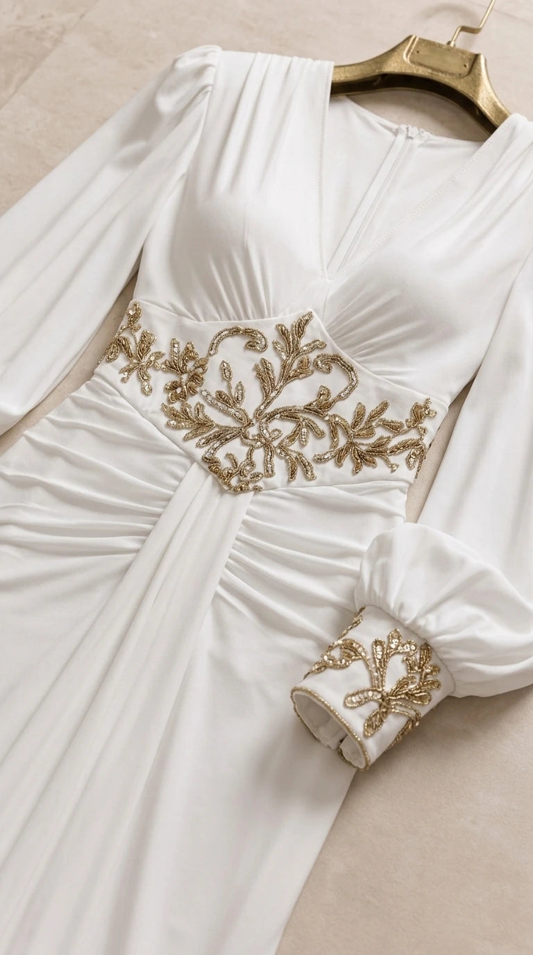 Close-up flat lay view of white evening dress showing gold embroidery on waist and sleeve cuffs