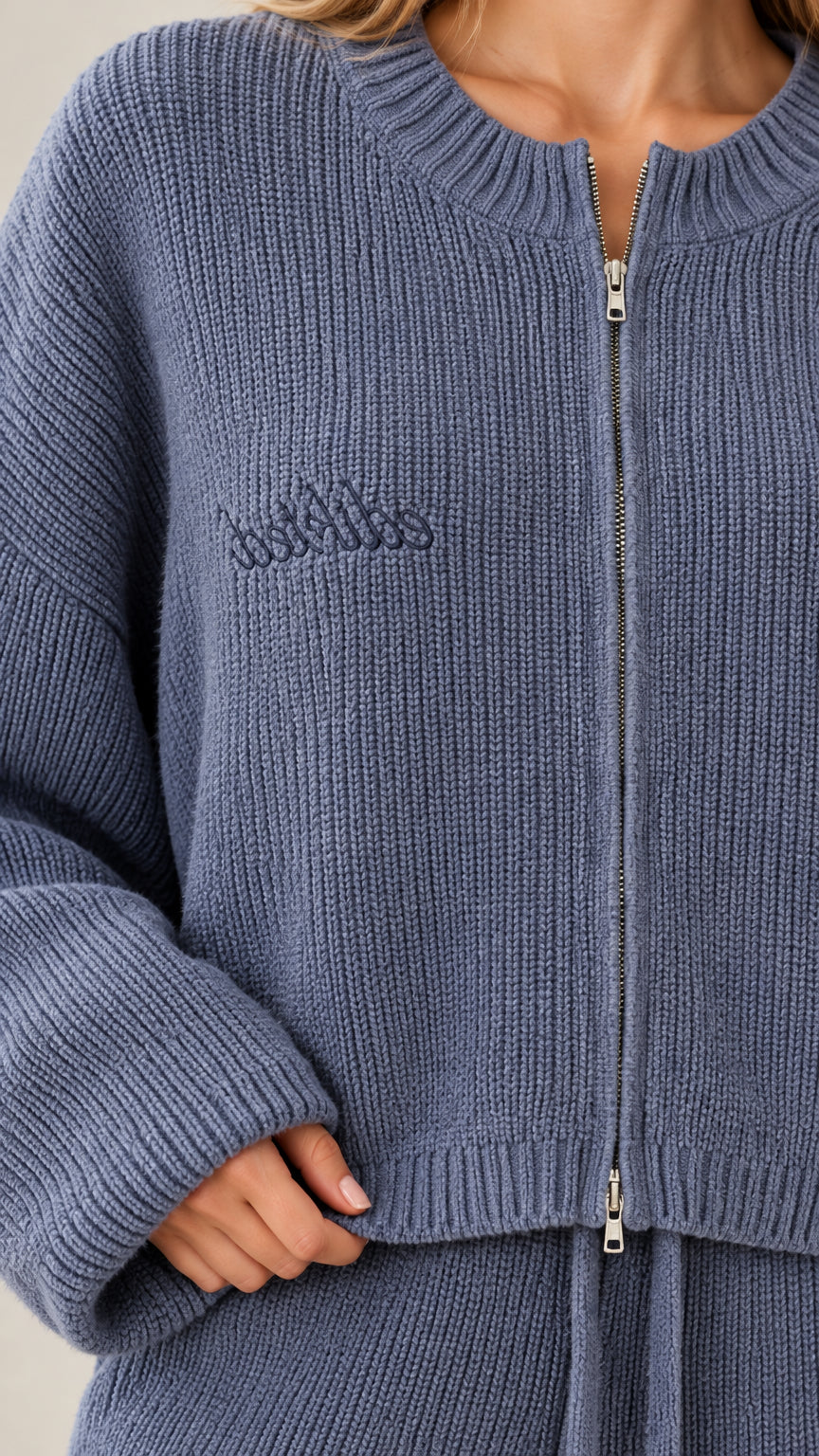 Close up view of Dusty Blue ribbed knit cardigan showing dual metal zipper and subtle chest embroidery
