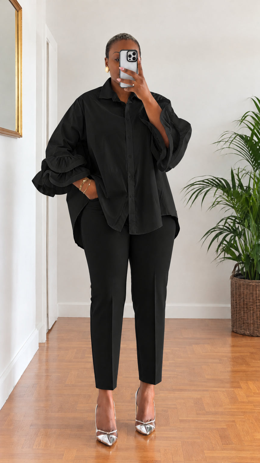 Full-length view of woman wearing black tiered ruffle sleeve button-down shirt with matching black trousers