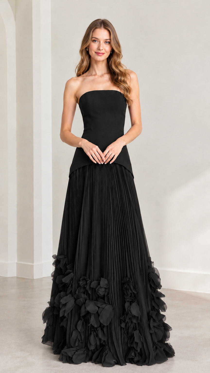 Front view of model wearing black strapless pleated maxi dress with petal trim