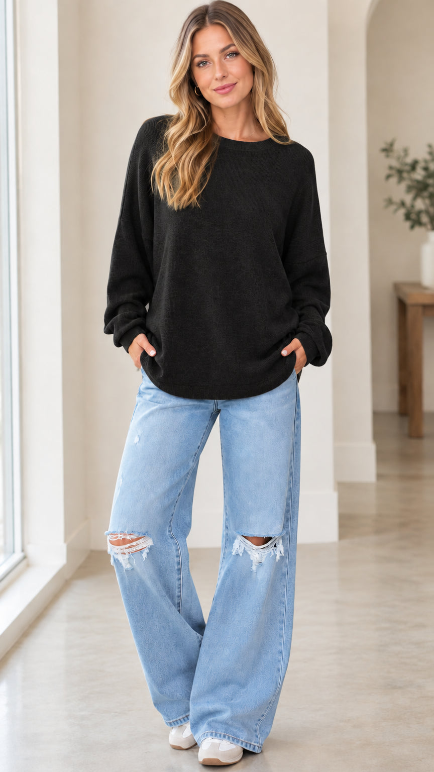 Front full view of woman wearing black relaxed crewneck knit pullover sweatshirt with wide-leg jeans