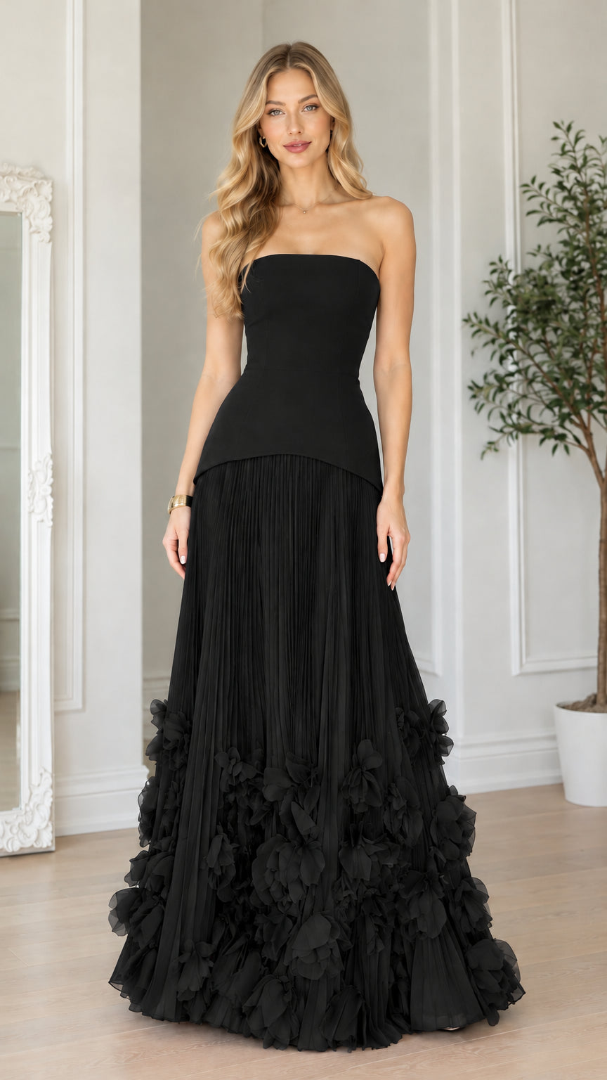 Front view of black strapless corset pleated maxi gown with 3D floral hem