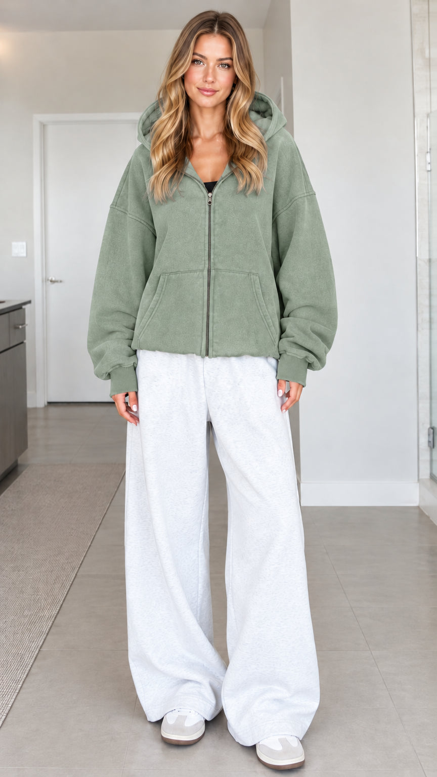Front view of a woman wearing a sage green oversized zip hoodie styled with white sweatpants