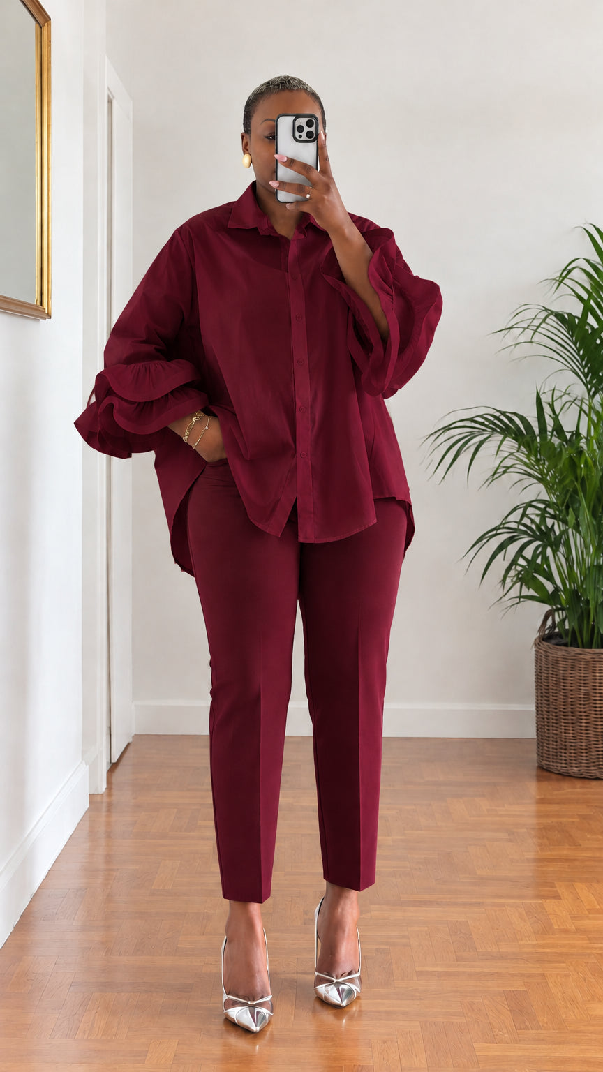 Full-length view of woman wearing rich burgundy tiered ruffle sleeve button-down shirt with burgundy trousers