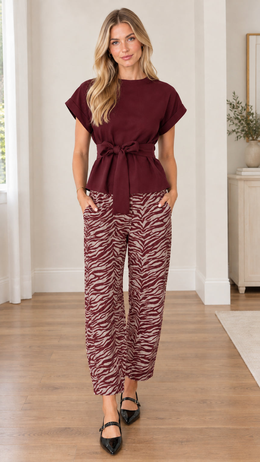 Front view of model wearing burgundy tie-waist blouse and burgundy zebra print pants