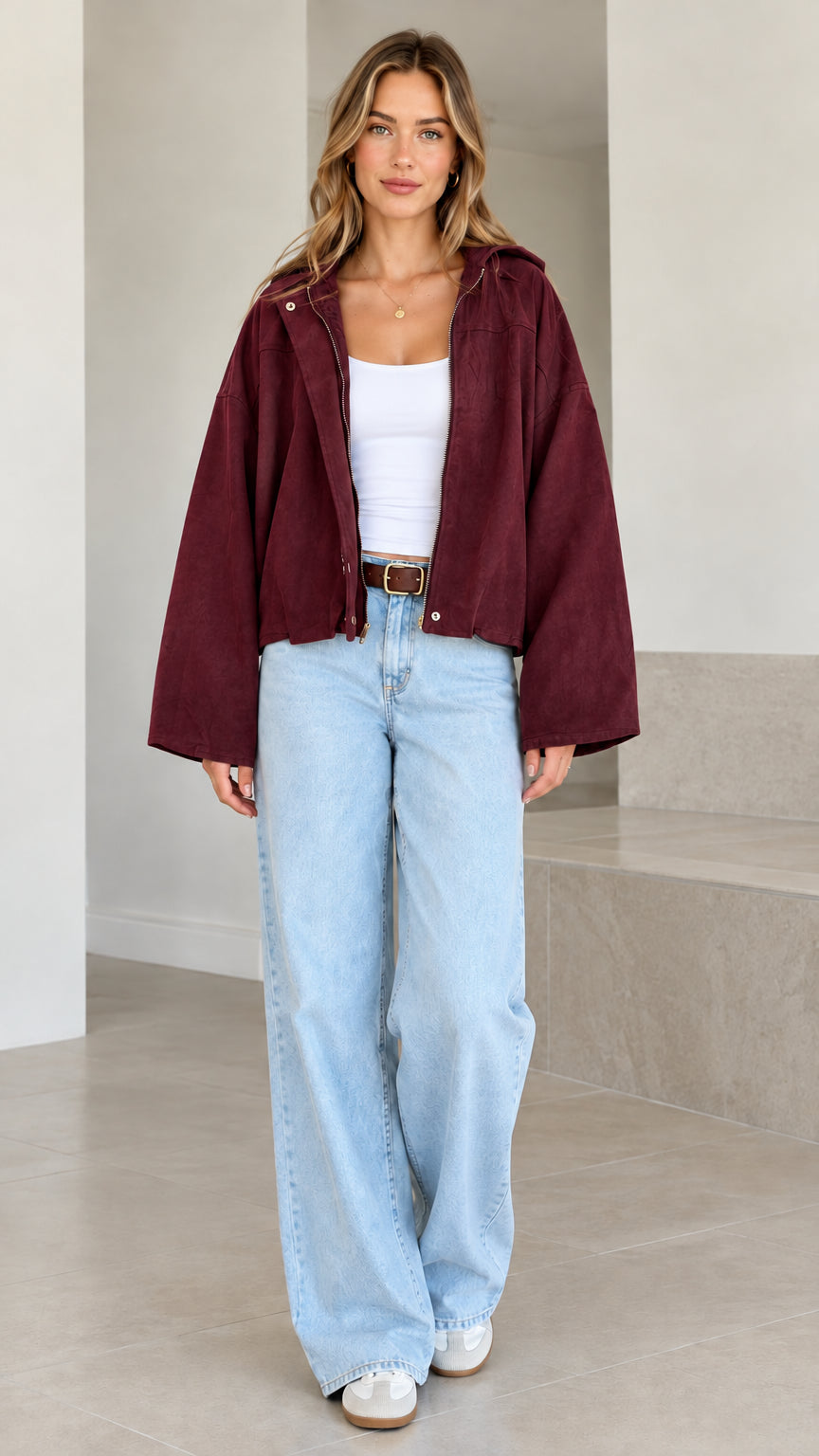 Model wearing burgundy red hooded cropped jacket styled over a white tank top