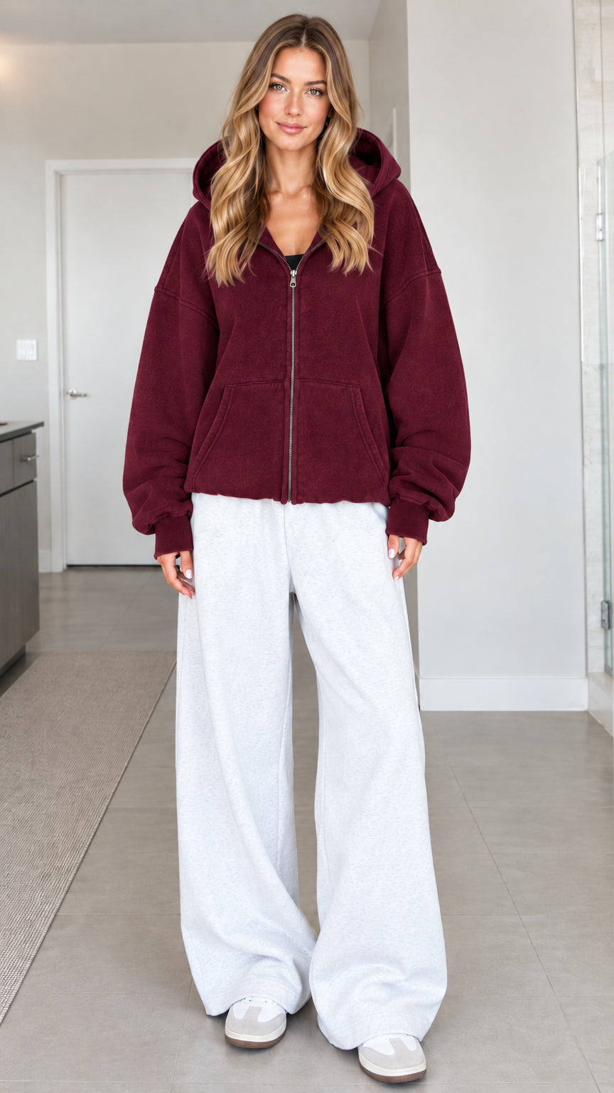 Front view of a woman wearing a burgundy oversized zip-up fleece hoodie with white sweatpants