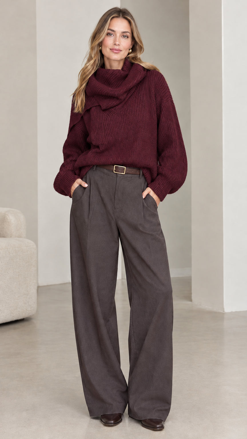 Front view of model wearing burgundy ribbed knit cowl neck sweater paired with grey trousers