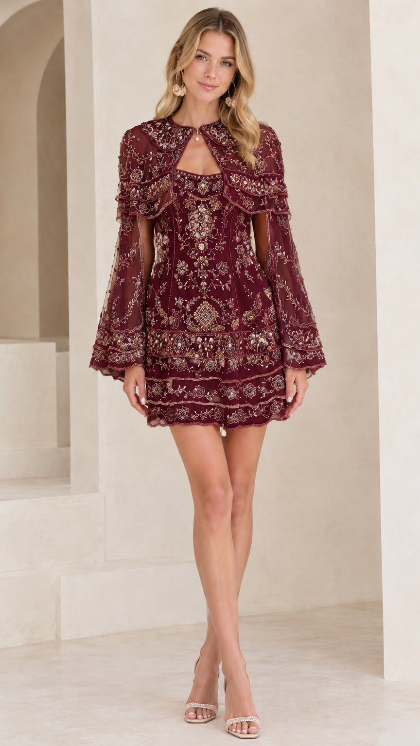 Front view of model wearing burgundy sequin embellished capelet mini dress