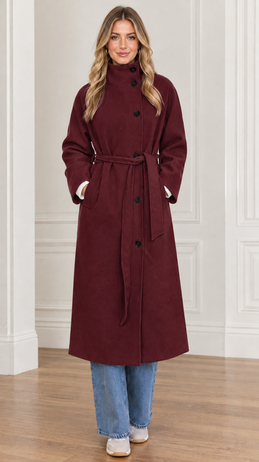 Front view of woman modeling burgundy long high neck trench coat with belt